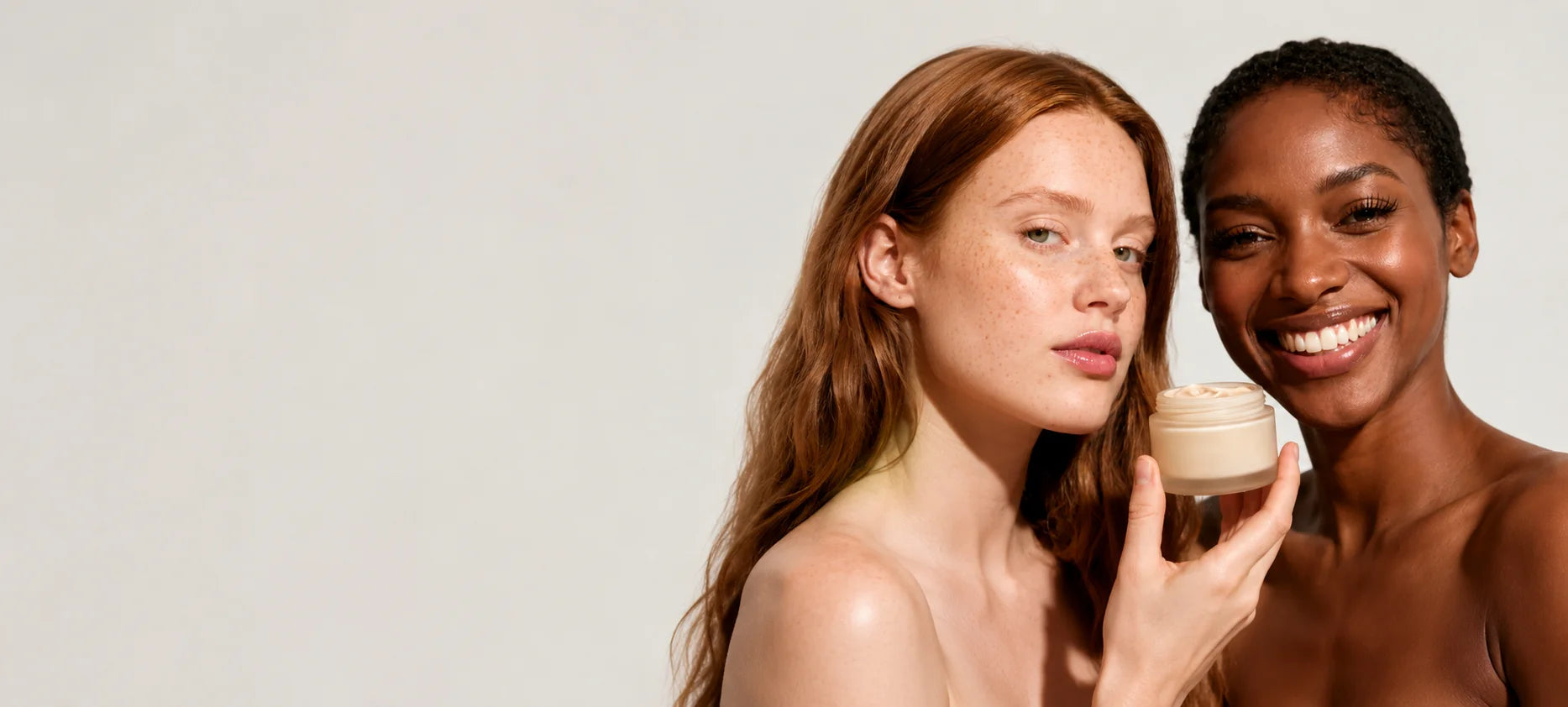 Two models holding a small jar of cream makeup against a plain light gray background.